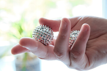 Silver metal magnetic balls in female hand. Spiky tool for hand massage.