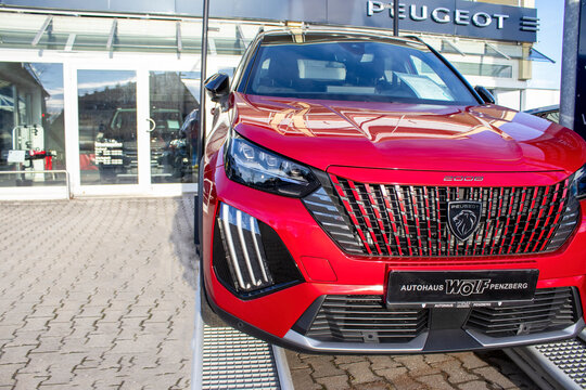 Penzberg, Germany, December 25, 2023: A modern red car against the background of the facade of the Peugeot car dealership. Store of a French car manufacturer