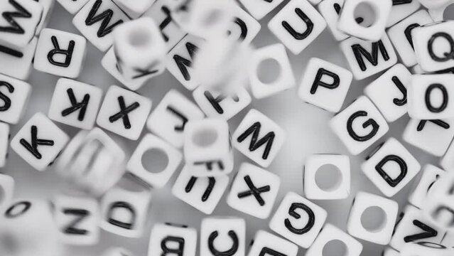 Close-up lot of white plastic decorative cubes with alphabet letters falling down moving randomly and mixing