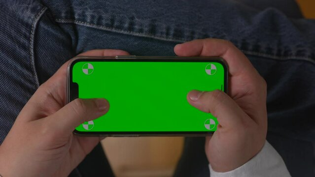 Close-up of hands holding smartphone with green screen