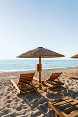 Wooden loungers await under rustic straw umbrellas on a sun-kissed beach, relaxation by the turquoise sea