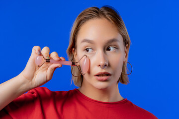 Teen girl with rose quartz stone roller on blue background. Facial self care