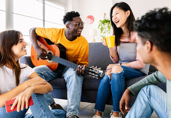 Diverse group of friends enjoying time together bonding at home. Millennial college students hanging out gathered in the living room at share flat. Youth community and friendship concept.