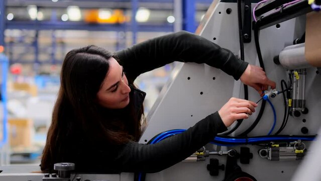 Young woman working in a factory. Employee using screwdriver.