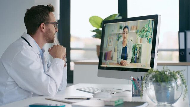 Video of mature male doctor talking in a video call with computer in the consultation.
