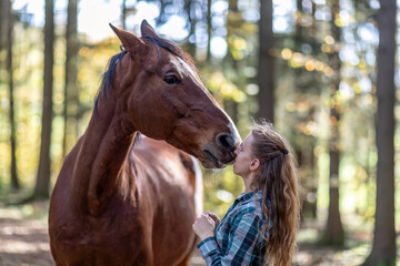 A young woman cuddle with her bay brown trotter horse in autumn outdoors