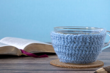 Cup of tea in woolen winter glass with open holy bible book on rustic wooden table. Close-up. Copy space. 