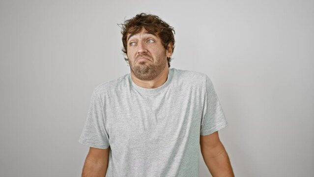 Baffled young man in t-shirt raises arms in clueless gesture, puzzled expression displaying doubt on isolated white background