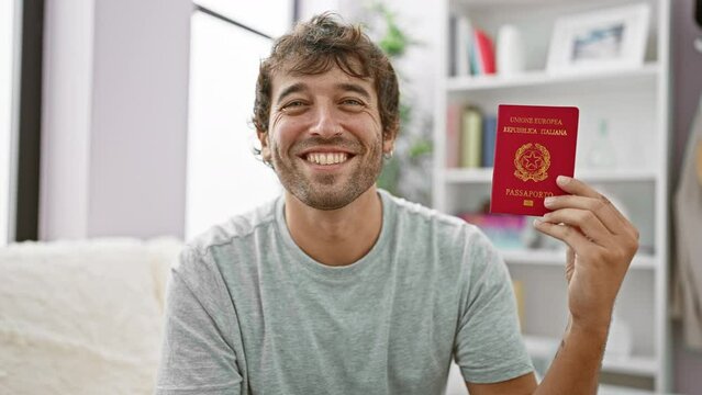Happy young man elated on his couch, confidently holding his italian passport, ready for a vacation adventure from the comfort of his home!