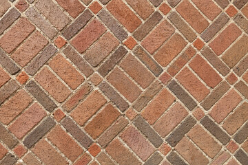 A diagonal red brick square pattern and texture. This side of a brick house shows detailed shapes out of the old and weathered bricks.