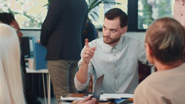 Concerned young male team lead brainstorms together with team in busy workplace.
