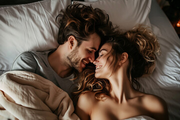 Young beautiful and loving couple wake up while lying on white pillows under the covers on soft white bed at the morning - obrazy, fototapety, plakaty