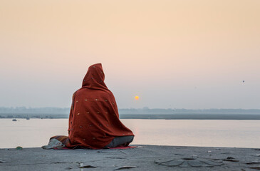 a man sits faced away from the camera along sacred varanasi river 
