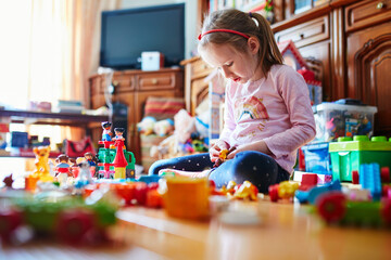 Adorable preschooler girl sitting on the floor and playing with colorful construction blocks