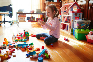 Adorable preschooler girl sitting on the floor and playing with colorful construction blocks - obrazy, fototapety, plakaty