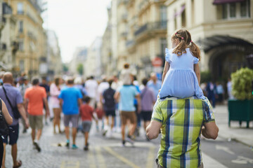 Father holding his daughter on shoulders and walking on street of Paris, France