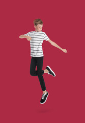 Teenage boy jumping on red background, full length portrait