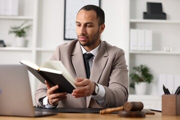 Serious lawyer reading book at table in office