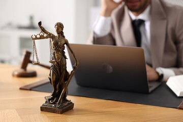 Lawyer working with laptop at table in office, focus on statue of Lady Justice