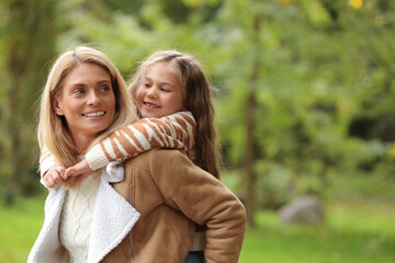 Fototapeta premium Happy mother walking with her daughter in autumn park, space for text