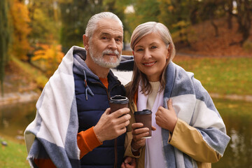 Affectionate senior couple with cups of coffee in autumn park