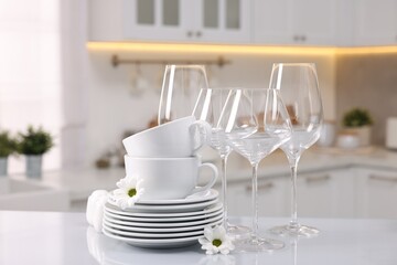 Set of clean dishware, glasses and flowers on table in kitchen