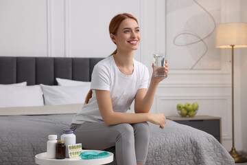Happy young woman holding glass of water near table with pills and measuring tape in room. Weight loss - Powered by Adobe