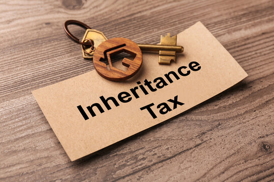 Inheritance Tax. Card and key with key chain in shape of house on wooden table, closeup