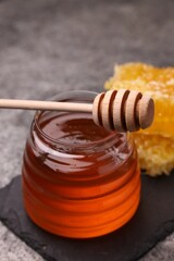 Sweet golden honey in jar and dipper on grey table, closeup