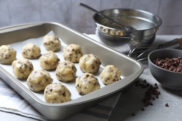 Baking pan with raw chocolate chip cookie balls on table, closeup