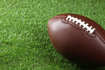 Leather American football ball on green grass, closeup. Space for text