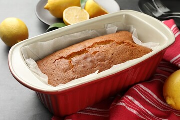 Tasty lemon cake in baking dish and citrus fruits on grey table, closeup