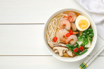 Tasty ramen with shrimps in bowl and chopsticks on white wooden table, top view. Space for text