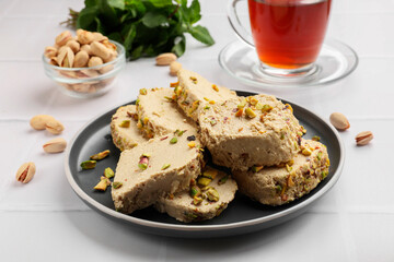 Tasty halva with pistachios served on white tiled table, closeup
