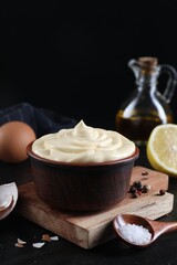 Fresh mayonnaise sauce in bowl and ingredients on black table, closeup