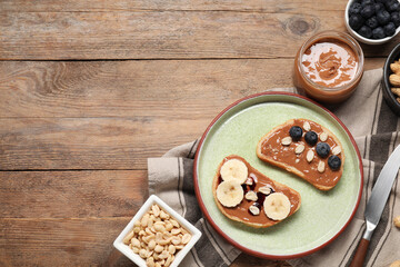 Toasts with tasty nut butter, banana slices, blueberries and peanuts on wooden table, flat lay. Space for text