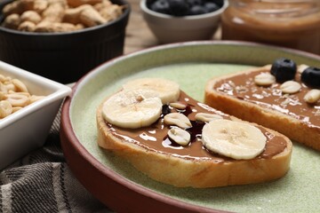 Toasts with tasty nut butter, banana slices, blueberries and peanuts on table, closeup
