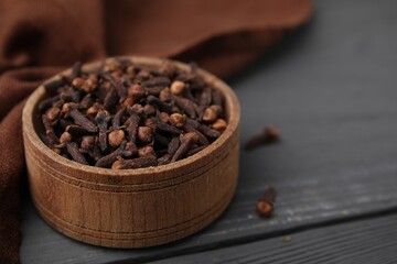 Aromatic cloves in bowl on grey wooden table, closeup. Space for text
