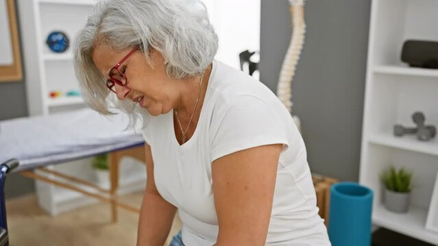 Mature woman with grey hair feeling knee pain at the rehab clinic.