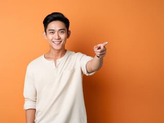 Portrait of asian man pointing and smiling isolated on orange background