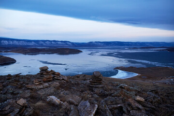 Beautiful view of Lake Baikal in winter at dawn. Pyramids of stones built by tourists on an open mountainside. The concept of travel, hiking and outdoor activities