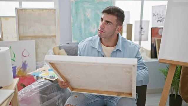 Handsome young hispanic man, deep in thought, masterfully drawing in a bustling art studio