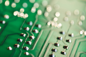 Conductor traces with silver drops of solder on a green electronic circuit. Computer board with electrically conductive circuits of an electronic circuit in the form of stripes in a blur.