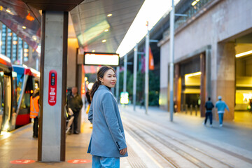 Asian woman waiting for tram at station in the city. Attractive girl tourist enjoy urban outdoor...