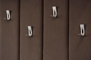 A soft wall upholstered with a furry brown fabric with silver hooks for clothes close-up with a...