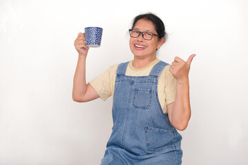 An Asian woman is holding a cup of hot drink while raising her thumb; cheerful, happy expression