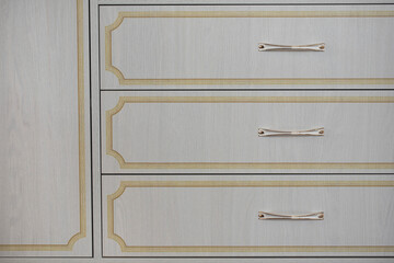 Background of drawer fronts in white color with vintage yellow frames drawings on the fronts in retro style. Close-up of a new cabinet with gilded handles. Photo printing drawing on furniture facades.