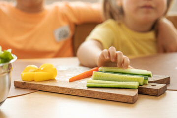 Obraz na płótnie Canvas Children take sticks of fresh sticks of carrots and cucumbers. Healthy eating.