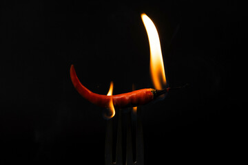 Chili pepper on fork with flames on black background. Burning red chili pepper. Slow motion