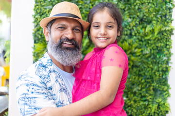 Fototapeta premium Senior looking Indian father wearing hat holding daughter and enjoying in shopping mall.